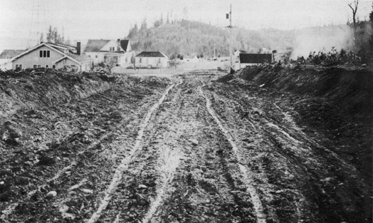 By 1922, employees were using automobiles to get to work causing base roads to deteriorate. In
the winter months, the
roads were mud holes and in the summer, dust. With no sidewalks, pedestrian journeys were no
less than ordeals. This photo, taken to the south on B Street, shows Quarters E and D.