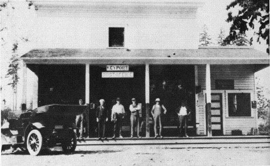 Photo with 6 people and a car in front of the Merchantile and Post Office.