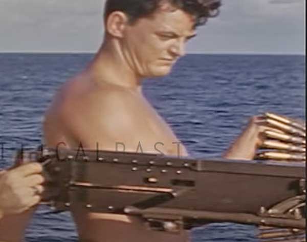 bare chested crew member feeding ammo with gun in foreground