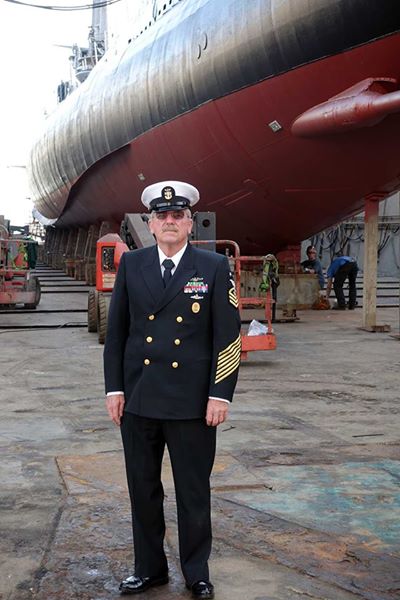 Charlie Butcher in his uniform with boat behind him.