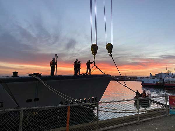 crane hook lifting bow chain with orange sky in the background