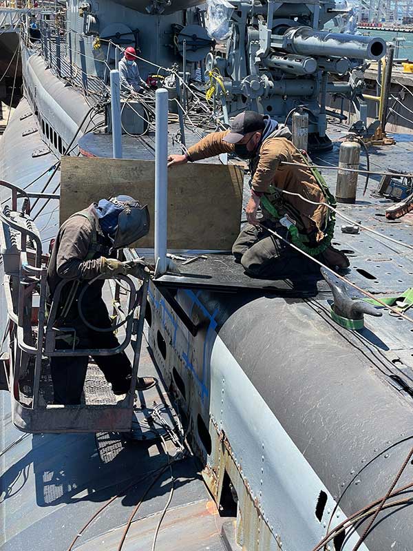 gun bolt on deck in background, workers welding stanchions on brow platform in foreground