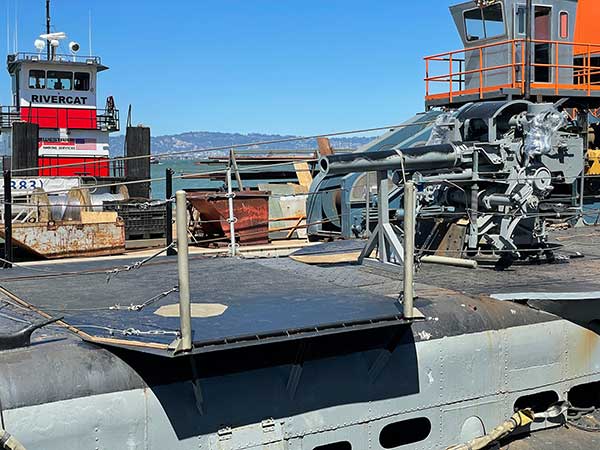empty brow landing platform and 5 inch gun in foreground with barge and tug in the background